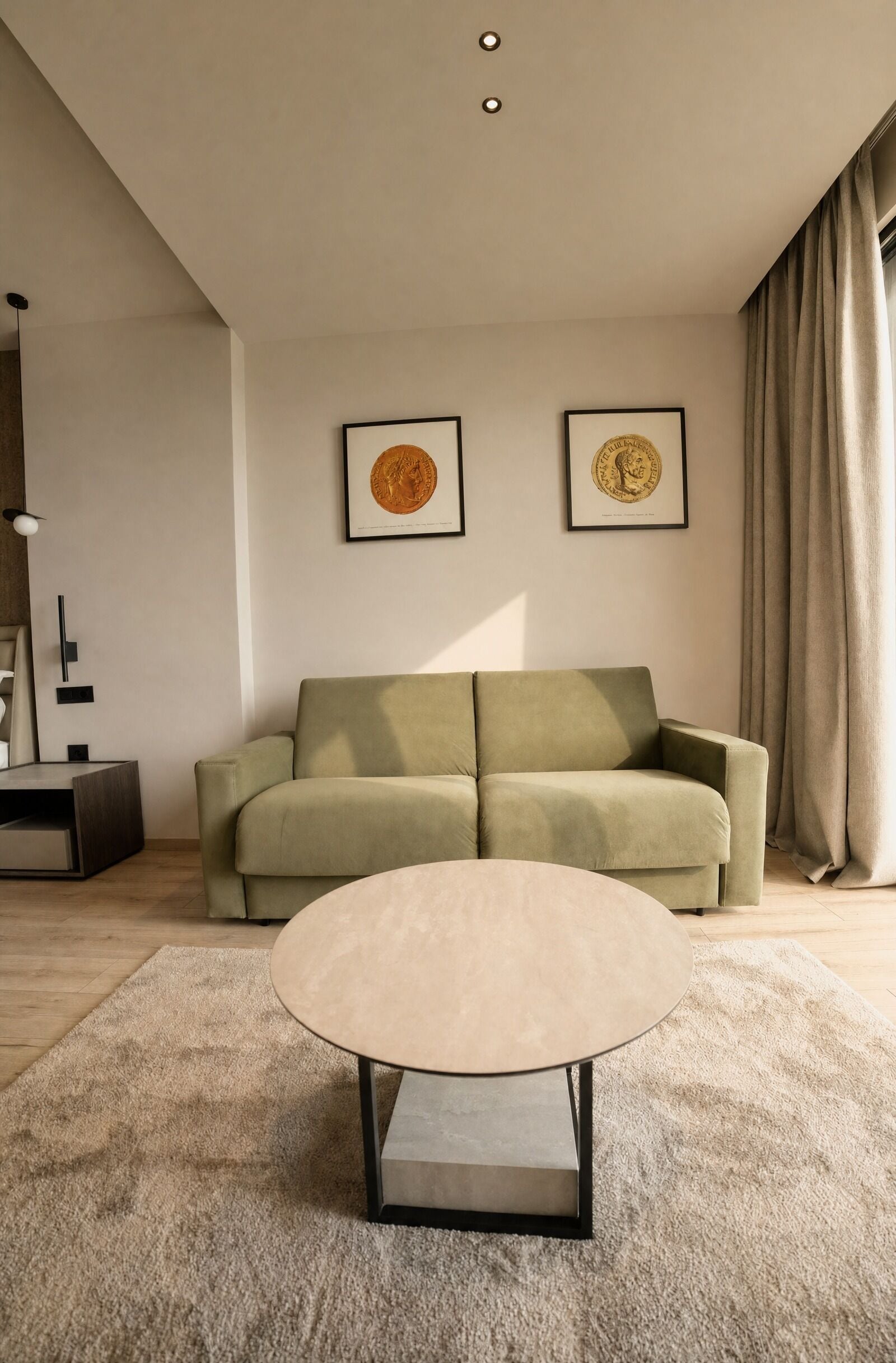 A modern living room with a green sofa, two framed pictures on the wall, and a round coffee table.