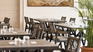 A restaurant interior with a large classical painting on the wall, wooden tables, and chairs. - CHAONIAN Hotel (Himare)