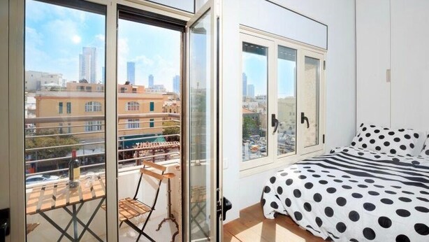 A bedroom with a bed, a window, and a balcony with a chair. - TLV Market Apartment (tel aviv)