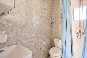 Een badkamer met een betegelde muur, een wit toilet, een douche met gordijn en een wastafel met kraan.