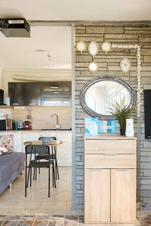 A modern living room with a stone wall, a round mirror, a wooden cabinet, a dining table with chairs, and a kitchen in the background. - pRETTyHome with private swimming pool,sea view,private parking,bbq,free wifi (χαλκιδικη)
