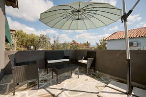 Een terras buiten met rieten meubels, een tafel en een grote parasol.
