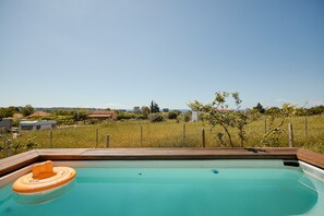 A swimming pool with a wooden deck, a floating ring, and a view of a grassy field and distant buildings. - pRETTyHome with private swimming pool,sea view,private parking,bbq,free wifi (χαλκιδικη)