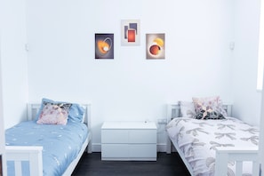Quarto com duas camas, mesa de cabeceira, cômoda e decoração na parede.