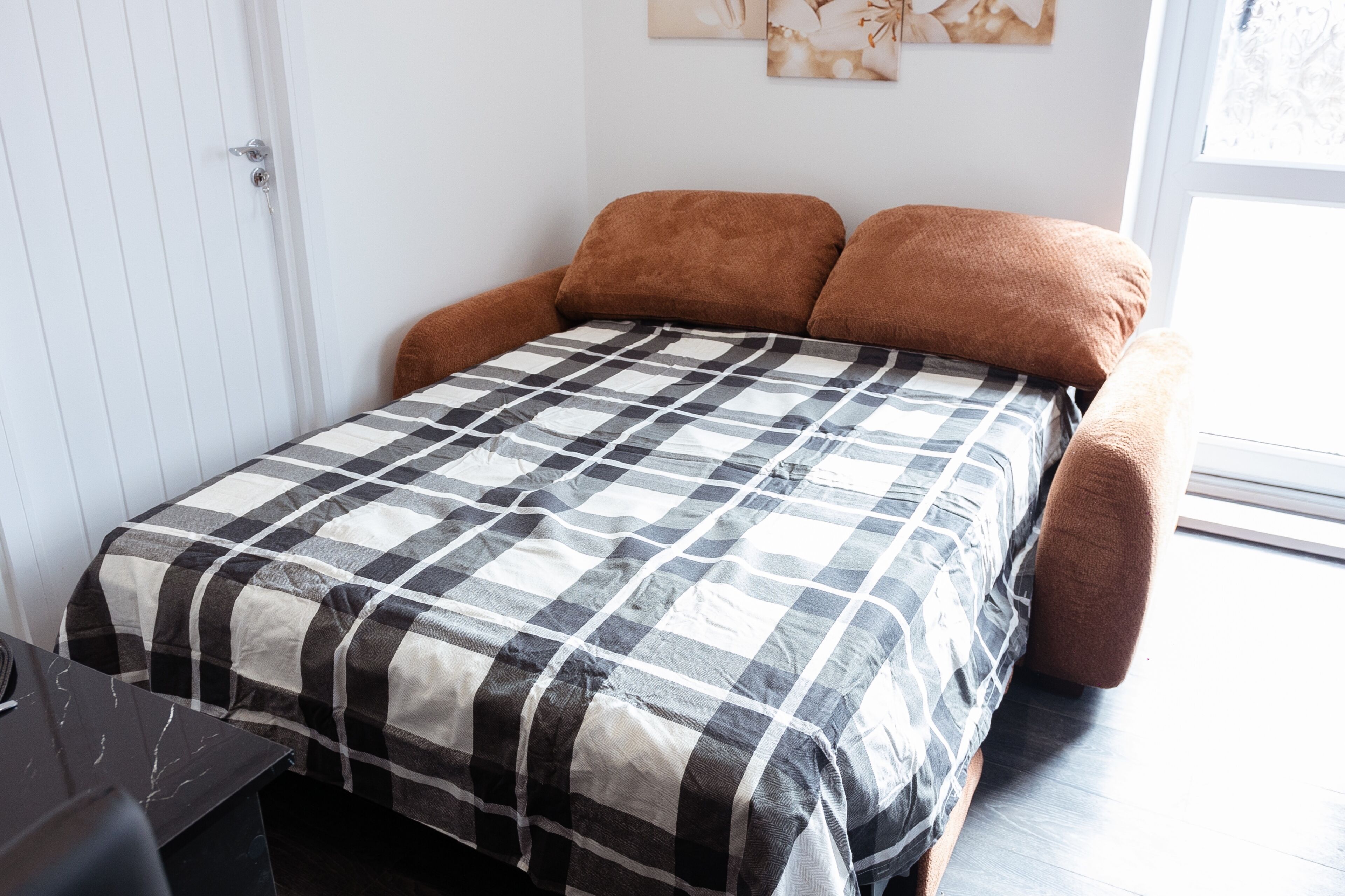 Una cama con colcha a cuadros, cabecero marrón y ventana con luz natural.