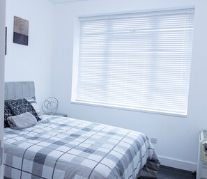 A bedroom with a bed, a window with blinds, a wall-mounted artwork, and a radiator. - 2 Bed Apartment Sleeps 4 - Free Parking, Near o2 (London)