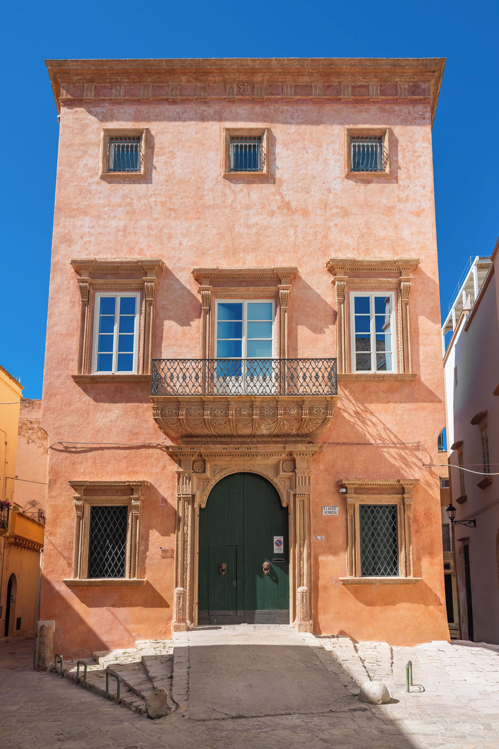 A pink building with a green door, a balcony with a metal railing, and a sign on the door.