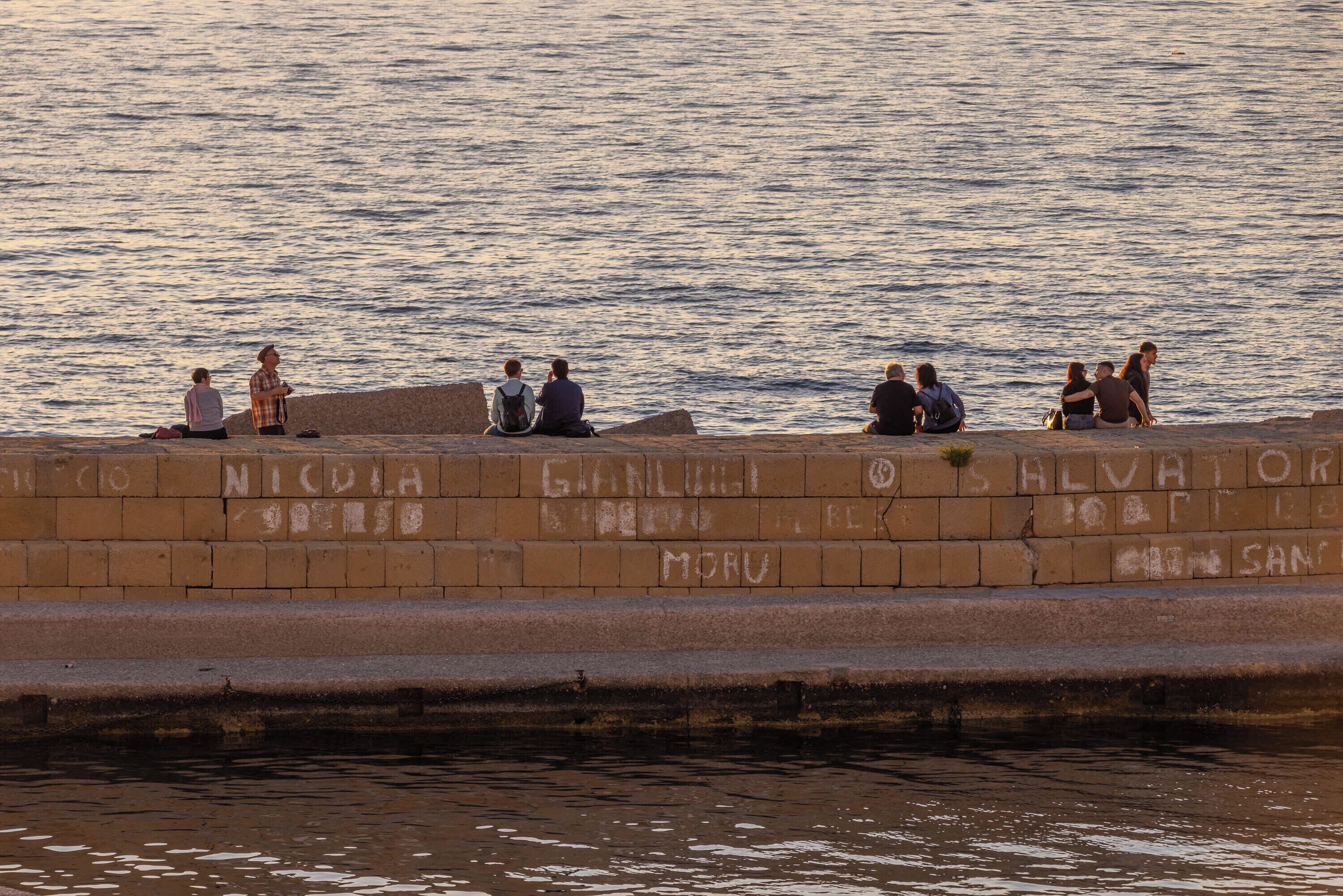 A waterfront promenade with people sitting on steps.