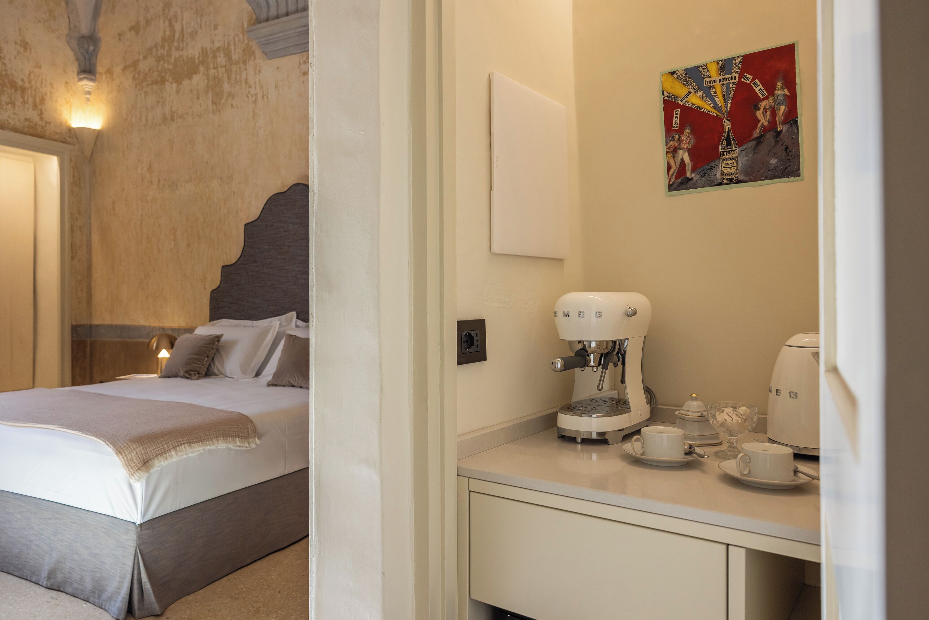 A hotel room with a bed, a coffee machine, and a small table with cups and a glass.