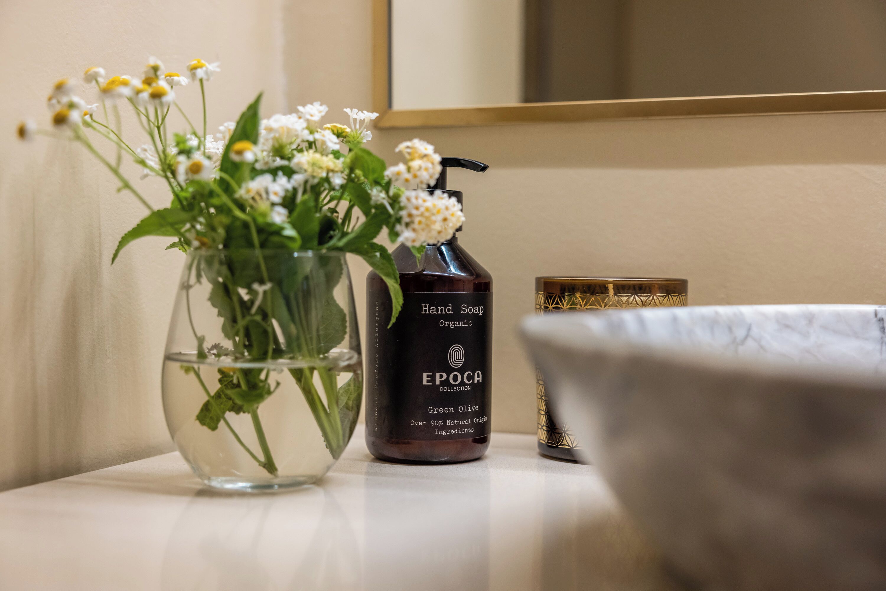 A bathroom vanity with a glass vase containing flowers, a bottle of hand soap, and a marble basin.