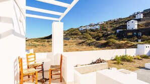 A terrace with white walls, a table, and two chairs. In the background, there is a hillside with white buildings. - Santorini's Welcoming Getaway - Blissful & Homely (Pori)