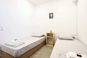 A small, clean room with two single beds, a bedside table with a lamp, and a small shelf. - Santorini's Welcoming Getaway - Blissful & Homely (Pori)