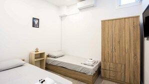 A small, modern room with two single beds, a wooden wardrobe, a flat-screen TV, and a small shelf. - Santorini's Welcoming Getaway - Blissful & Homely (Pori)