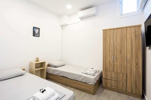 A small, modern room with two single beds, a wooden wardrobe, a flat-screen TV, and a small shelf. - Santorini's Welcoming Getaway - Blissful & Homely (Pori)