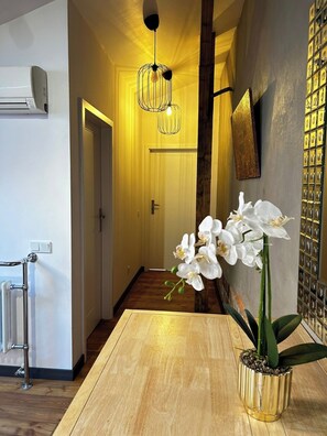 A hallway with a wooden floor, a white door, a wall-mounted air conditioner, a hanging light fixture, and a potted orchid on a wooden table. - Florianska DeLux Annex 2-bedroom apartment with AC in Old Town Kraków (Kraków)