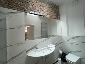 Een badkamer met een marmeren wastafel, een spiegel, een toilet en een bakstenen muur.