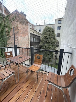 Een balkon met houten meubels, een metalen hekwerk en uitzicht op gebouwen en bomen.