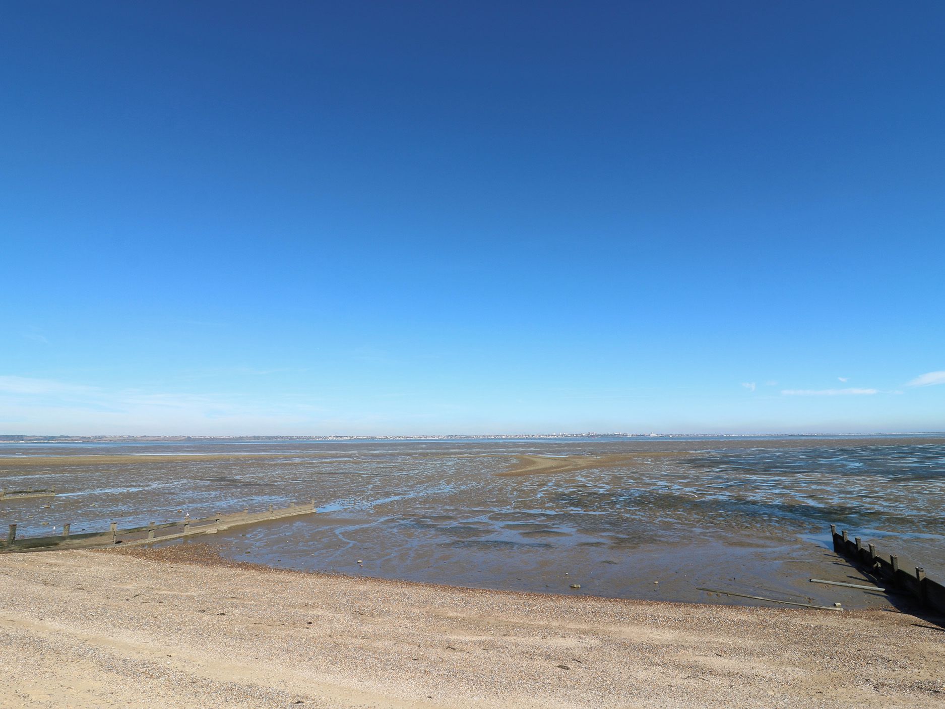 Un paysage côtier avec un ciel dégagé, une plage de sable et une côte lointaine.