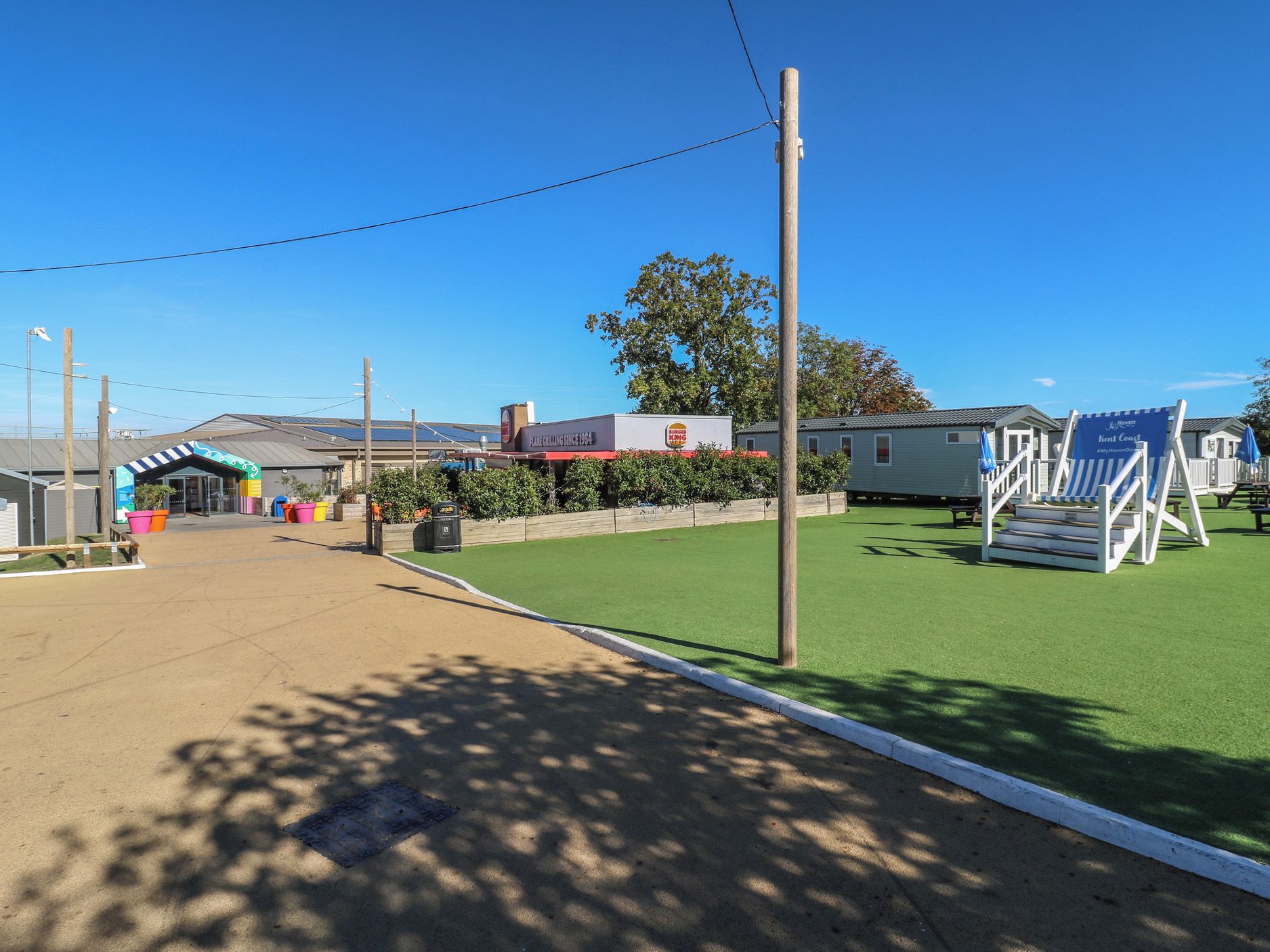 Un estacionamiento con una zona de césped artificial verde, un restaurante Burger King y una fila de sillas de playa.