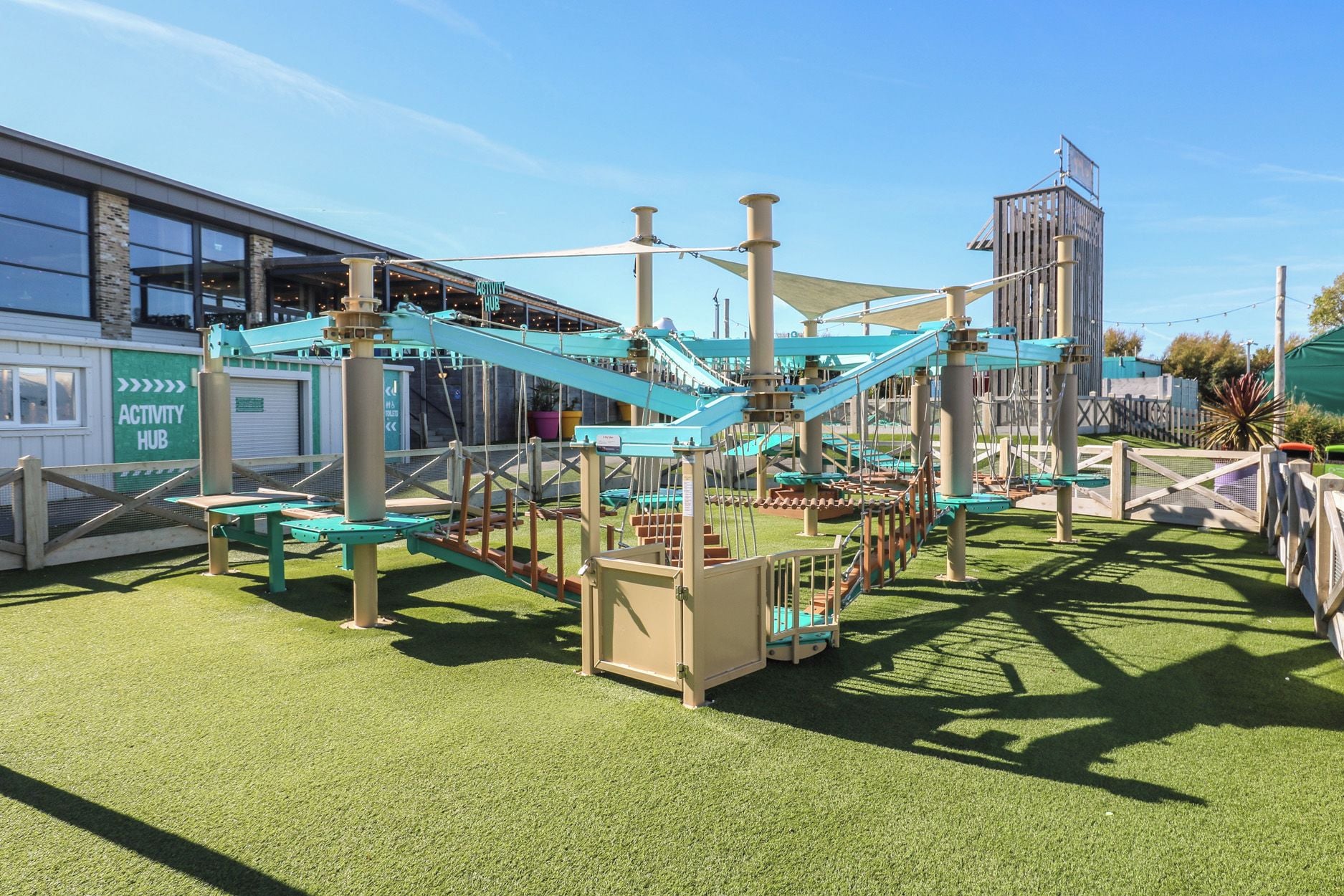 Ein Spielplatz im Freien mit Klettergerüsten und Rutschen, umgeben von einem eingezäunten Bereich mit künstlichem Rasen.