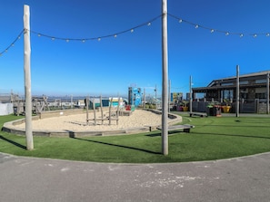 Una zona costanera amb una platja sorrenca, un edifici blau amb la façana 'The Shop' i un restaurant amb terrassa.