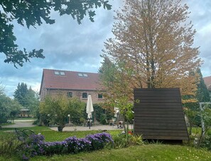 Ein Backsteinhaus mit Ziegeldach, Außenbestuhlung und einem Garten mit violetten Blumen.