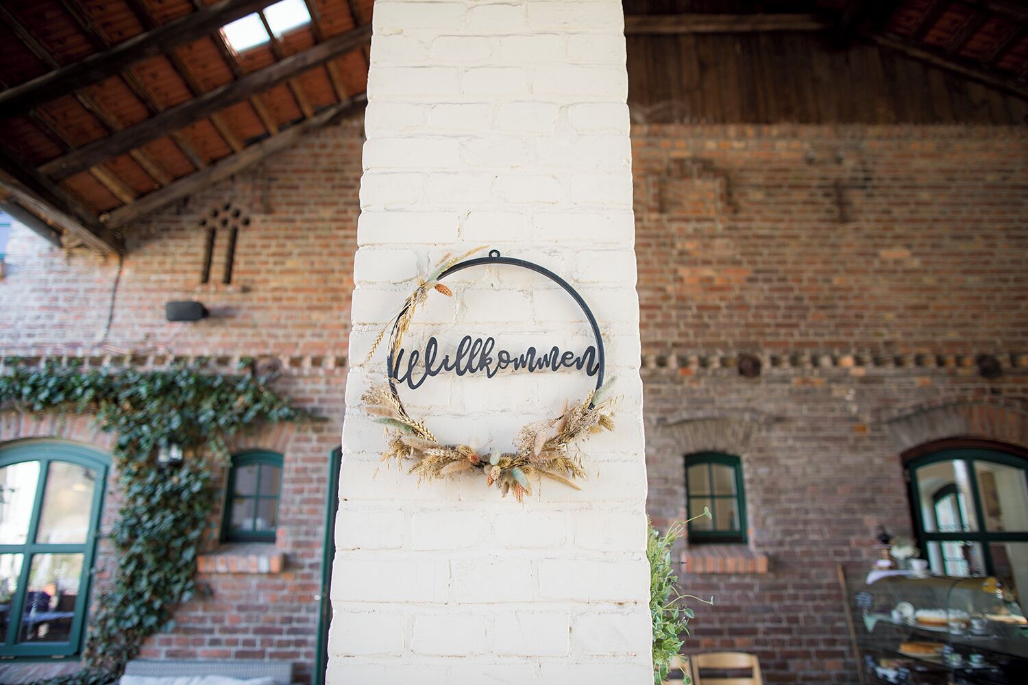 A white brick wall with a 'Willkommen' sign and a wreath.