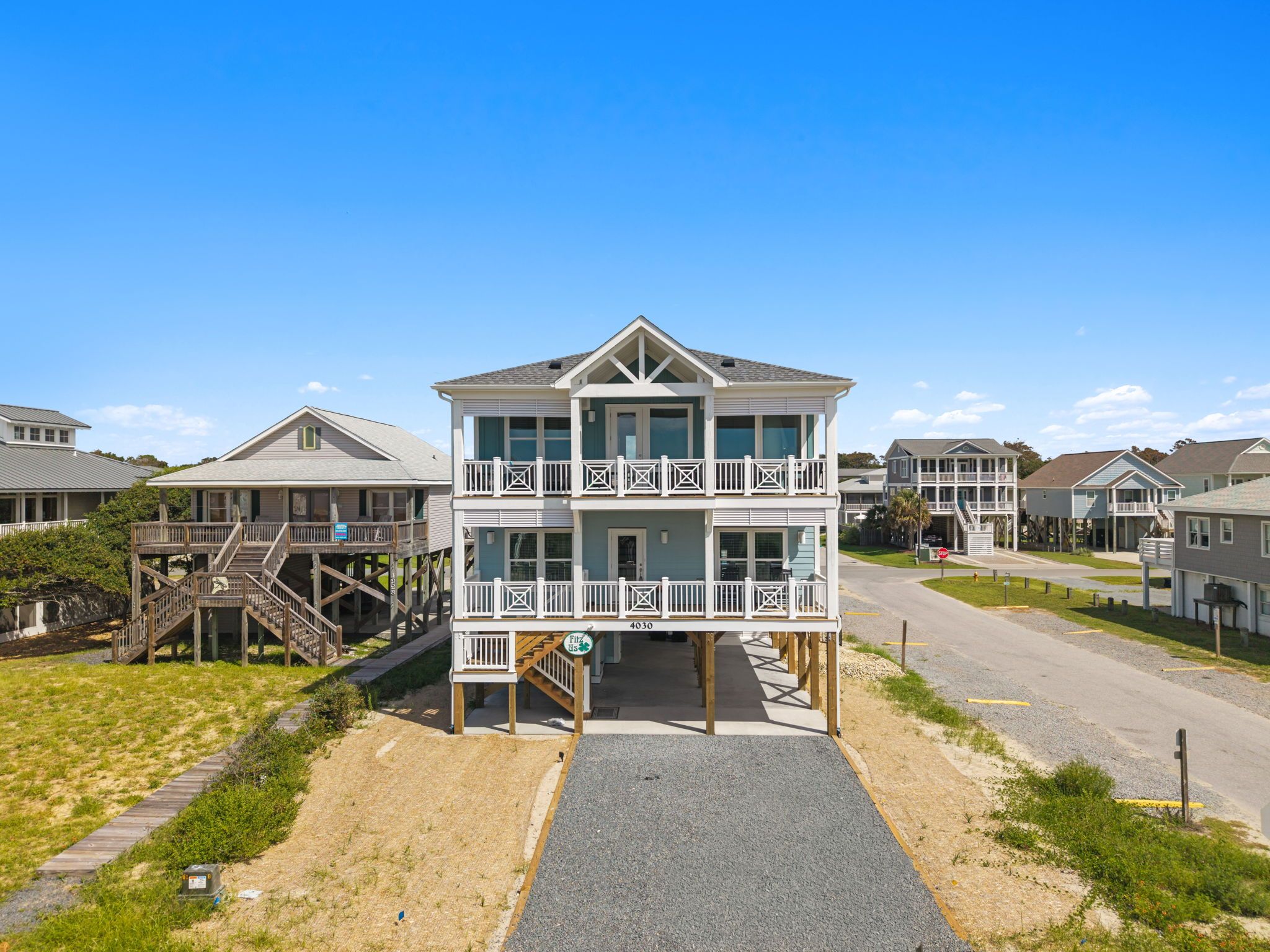 A two-story beachfront property with a balcony, a wooden deck, and a clear sky.