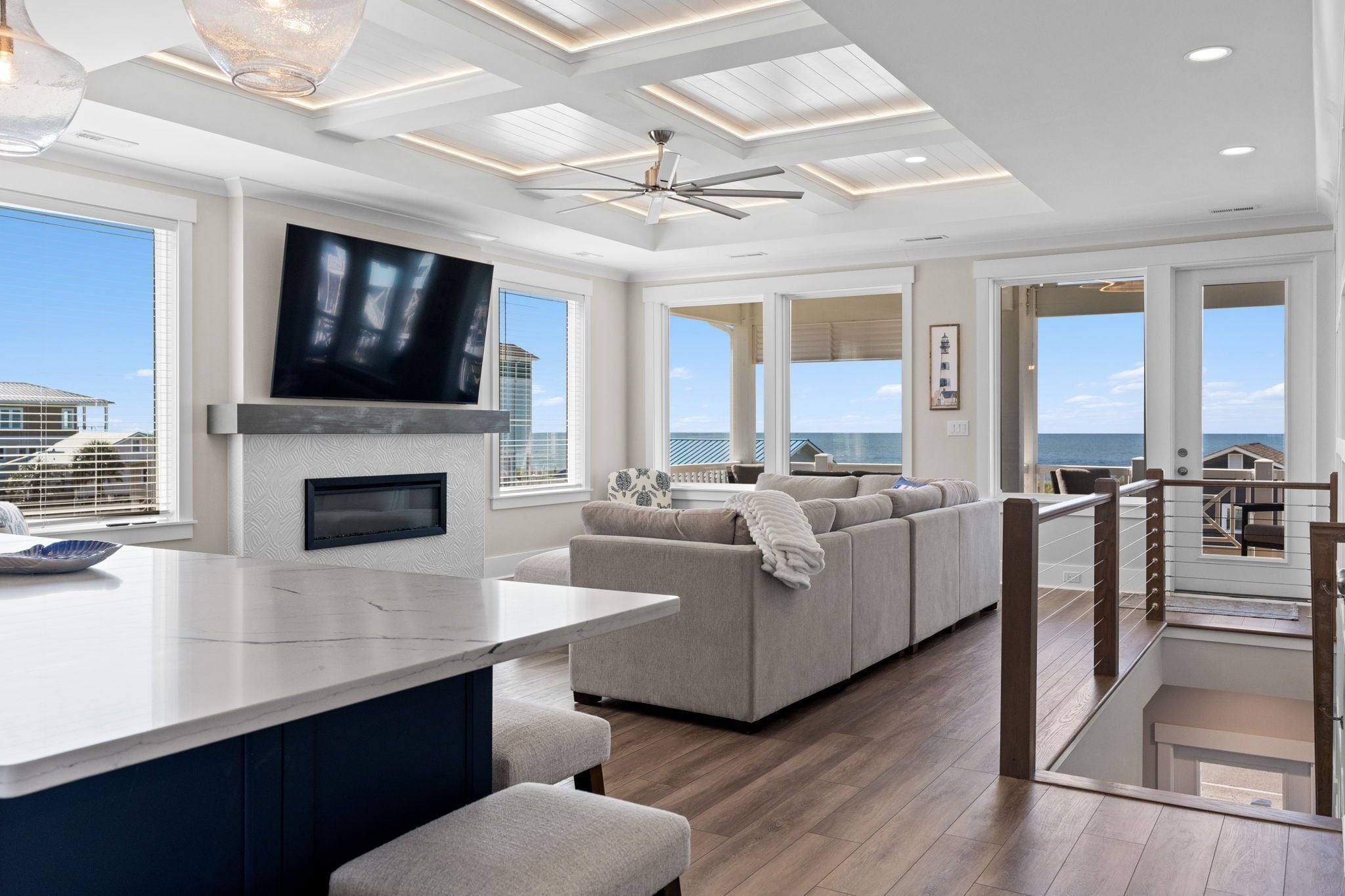 A modern living room with a large TV, a fireplace, a sofa, and a view of the ocean.
