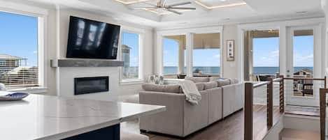 A modern living room with a large TV, a fireplace, a sofa, and a view of the ocean.