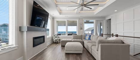 A modern living room with a fireplace, large windows, and a ceiling fan.