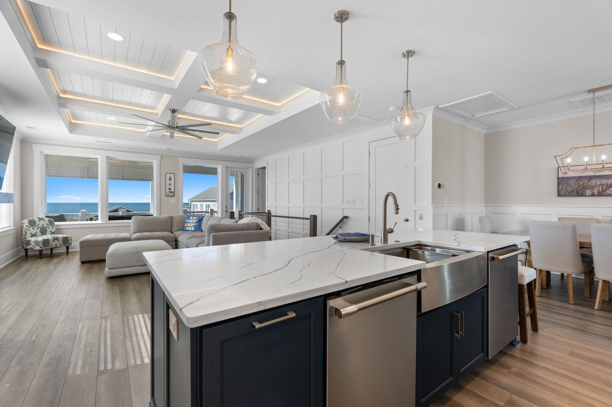 Une cuisine moderne dotée d’un grand îlot central, d’appareils électroménagers en acier inoxydable et de luminaires suspendus.