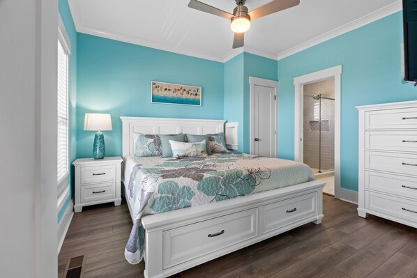 Une chambre à coucher comprenant un lit, des tables de chevet, une commode, un ventilateur de plafond et un espace douche.