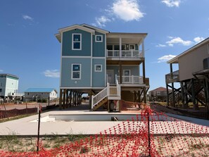 Ein mehrstöckiges Strandhaus mit Balkon, überdachter Veranda und Holzterrasse.