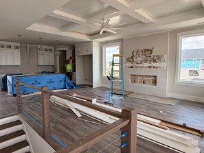 Ein Zimmer im Bau mit freiliegenden Wänden, einem Deckenventilator und Blick auf ein blaues Haus.