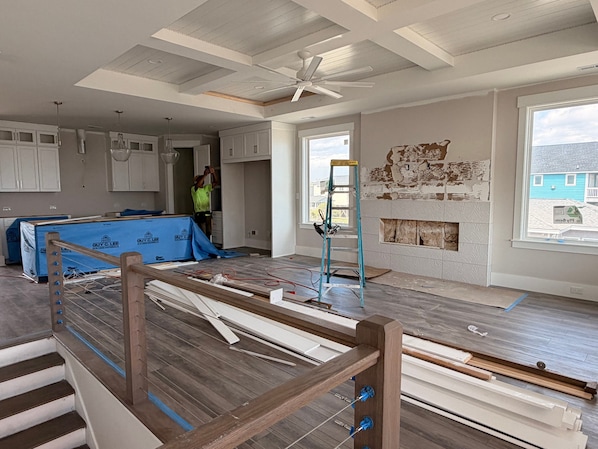 Ein Zimmer im Bau mit freiliegenden Wänden, einem Deckenventilator und Blick auf ein blaues Haus.