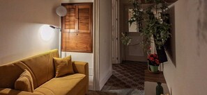 Une pièce avec un canapé, une lampe fixée au mur, une porte en bois et une plante en pot.