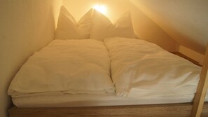 Ein Bett mit weißer Bettwäsche und einem hölzernen Kopfteil in einem Raum mit schlichten Wänden.
