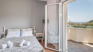 Un dormitorio con cama, mesita de noche, cajón, puerta de cristal que da a un balcón y vistas al paisaje.