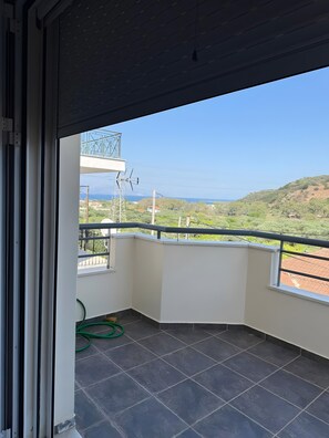 A balcony with a view of the sea and hills, a green hose, and a metal railing. - Apartment 'Family Home' with Sea View, Wi-Fi and Air Conditioning (Agios Konstantinos)
