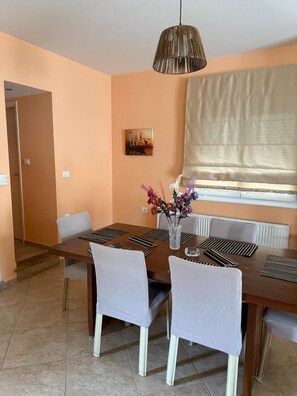 A dining area with a wooden table, striped chairs, a vase with flowers, a hanging light fixture, and a painting on the wall. - Apartment 'Family Home' with Sea View, Wi-Fi and Air Conditioning (Agios Konstantinos)