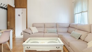 Un salon avec un canapé beige, une table basse blanche, une porte en bois et une fenêtre avec des rideaux.