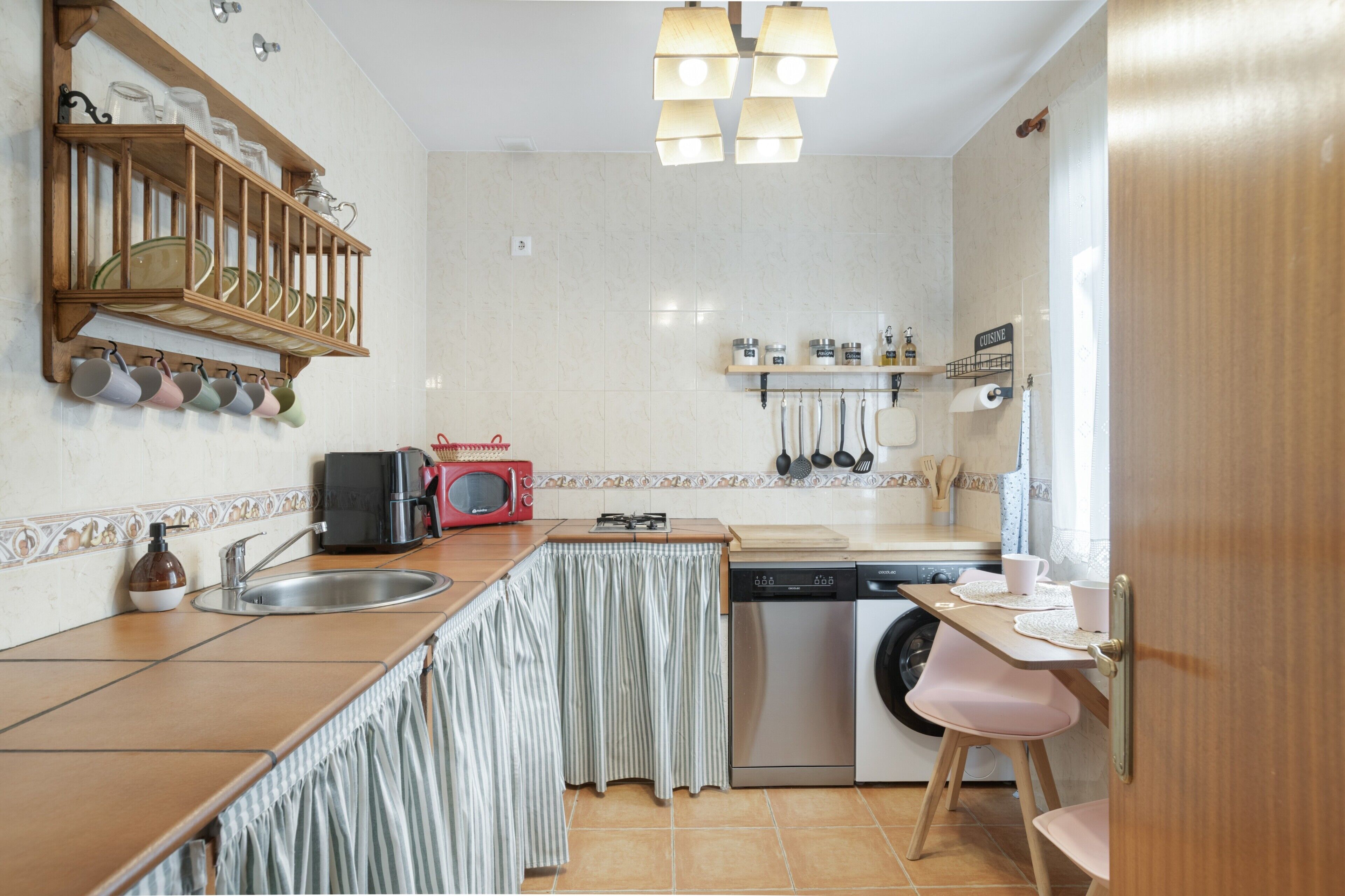 A compact kitchen with a sink, a microwave, a dishwasher, and a small dining area with a chair.
