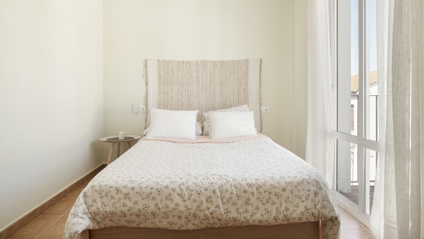 Une chambre à coucher avec un lit, une table de chevet, une fenêtre avec des rideaux et une vue sur les bâtiments à l’extérieur.