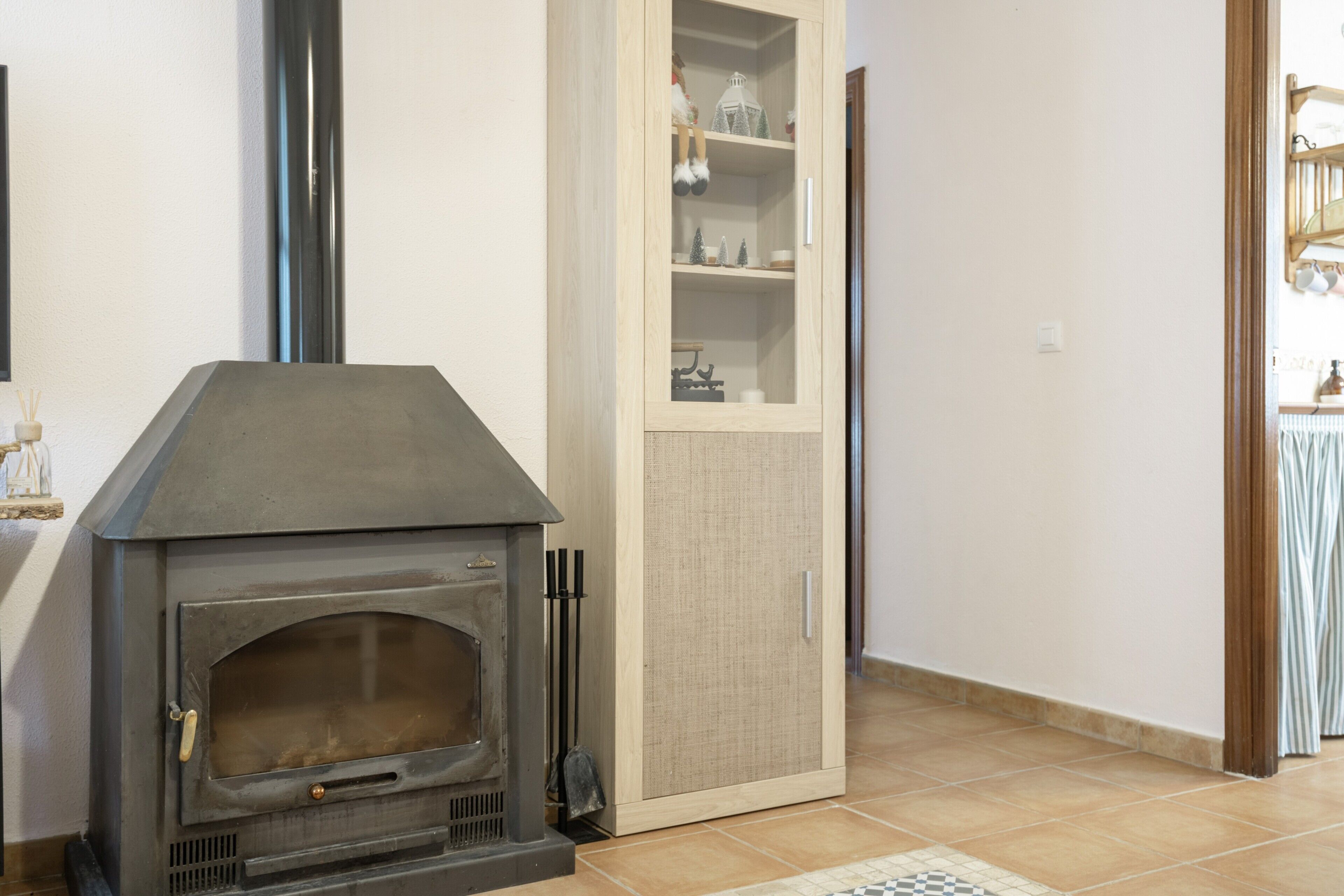 Une pièce dotée d’un poêle à bois, d’une armoire aux portes vitrées et d’un sol carrelé.