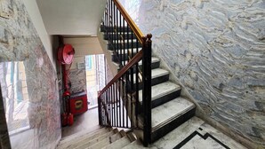 A marble staircase with a wooden handrail and black balusters, leading to a landing with a red fire extinguisher and a red box. - Anandaloke Guest House (Kolkata)