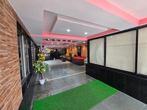 Un pasillo con alfombra verde, una planta en maceta y una recepción con sofá y sillón rojo.
