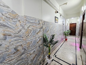 Um corredor com paredes de mármore, plantas em vasos e uma porta ao fundo.