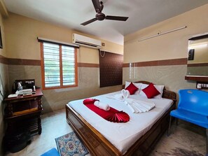 Habitación de hotel con cama, escritorio, silla, aire acondicionado y ventilador de techo.