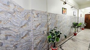 A hallway with marble walls, potted plants, and framed pictures. - Anandaloke Guest House (Kolkata)